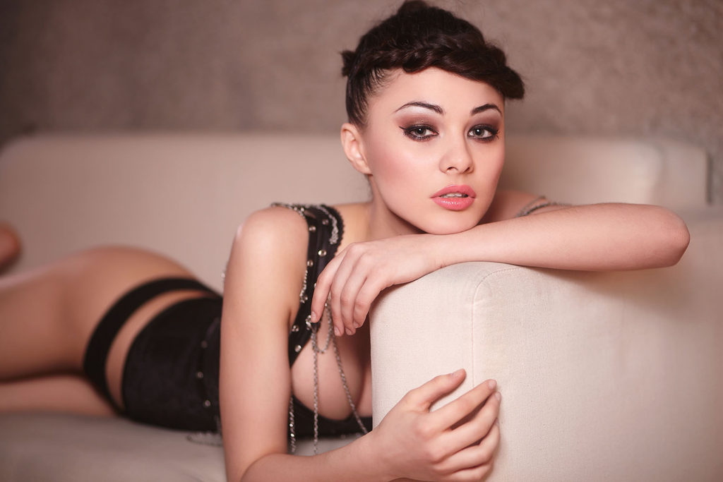Beautiful sexy fashion girl in black corset lying on the sofa indoors bright makeup and hairstyle